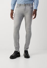 Šedé džíny úzkého střihu s vybledlým vzhledem, opatřené předními kapsami a poutky na opasek, doplněné černými koženými botami. Hladká textura a střihaný design.