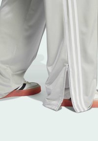 Harmaat urheiluhousut, joissa on kolme valkoista raitaa, sivuvetoketju ja yhdistettynä retrotennareihin, joissa on punainen pohja ja mustat yksityiskohdat.