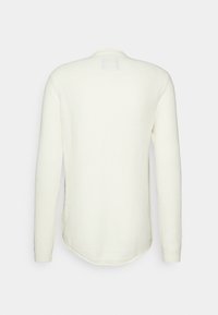 Pull en maille blanc à manches longues vu de dos, avec un ourlet arrondi et un motif de tissu texturé.