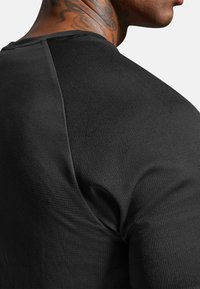 Černá košile s krátkými rukávy z texturované tkaniny s žebrovaným vzorem a přiléhavým střihem. Viditelný šev na rameni.