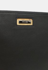 Borsa tote in pelle nera con superficie texture; presenta una toppa rettangolare con uno sfondo dorato e testo in rilievo. Chiusura con zip.