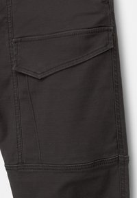 Mörkgrå tyg cargo-byxor med en texturerad yta, med en sned ficka och detaljerad sömnad längs sömmarna.