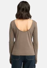 Langarmshirt in Olivgrün mit tiefem Rückenausschnitt und glatter Textur. Kombiniert mit dunklen Denim-Hosen.