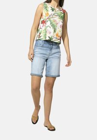 Mujer vistiendo una blusa sin mangas de flores, shorts de mezclilla azul claro con dobladillo enrollado y sandalias de piel color beige caminando hacia adelante.