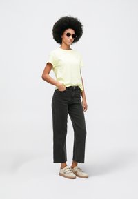 Ανοιχτό κίτρινο βαμβακερό μπλουζάκι, μαύρα τζιν ψηλής μέσης και μπεζ αθλητικά παπούτσια. Τα αξεσουάρ περιλαμβάνουν σκούρα γυαλιά ηλίου και φυσικό afro χτένισμα.