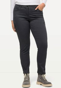 Dunkelgraue, slim-fit Cargo-Hosen mit einem Reißverschluss-Seitentasche, leichtem Stoff und elastischem Bund. Kombiniert mit grauen Knöchelstiefeln.