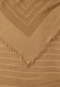 Eșarfă maro cu margine franjurată, model geometric subtil și text care spune „BOSS” într-o nuanță mai deschisă pe material.