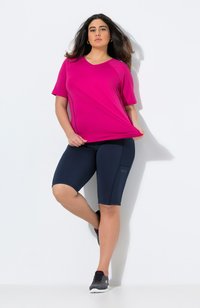 Vaaleanpunainen urheilupaita, jossa on lyhyet hihat ja V-kaula-aukko, yhdistettynä tummansinisiin pyöräilyshortseihin, joissa on struktuurisia yksityiskohtia. Tummat lenkkitossut täydentävät asua.