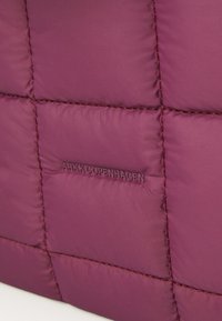 Burgunderfarget puffeveske med quiltet design, med glatt stoff, kontrasterende sømmer og preget "ARKK.COPENHAGEN" logo detalj.