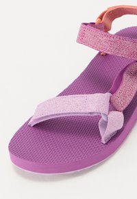 Sandálias roxas com solas de borracha texturizadas, apresentando duas tiras ajustáveis em tons de roxo claro e rosa. Projetadas para conforto e estabilidade.