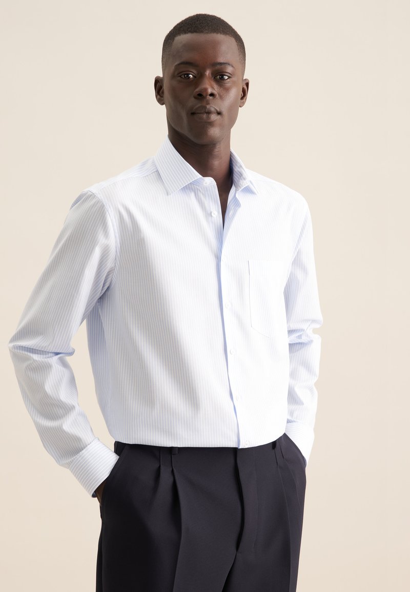 Camicia a righe blu chiaro con bottoni, realizzata in misto cotone, caratterizzata da maniche lunghe, taschino sul petto e colletto classico, abbinata a pantaloni scuri.