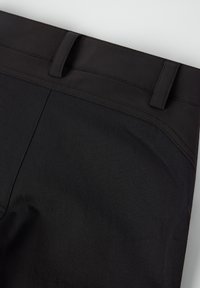 Close-up van de tailleband van zwarte broek en bovenste stof die riemlussen en gedetailleerde stiksels tonen op zowel een gladde als een gestructureerde stof.