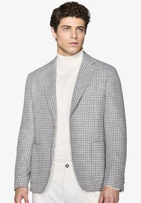 Grå og hvid houndstooth-mønstrede blazer med en notch-lapel, to-knap lukning og to forlommer, båret over en hvid turtle-neck.