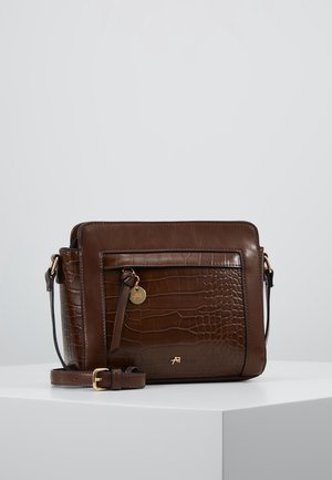 Brun lædertaske med krokodilletekstur, forreste lynlåslomme, guldfarvet logohalskæde og justerbar rem på hvidt displayunderlag.