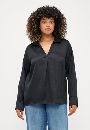 Blusa de satén negra con escote en V y mangas largas, que presenta pequeños puntos plateados y un corte relajado. Combinada con pantalones de mezclilla azul claro.