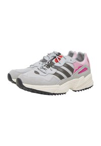 Lysegrå atletiksk shoes med teksturert stoff og semsket overdel, med tre mørkegrå striper, rosa detaljer og en robust svart såle.