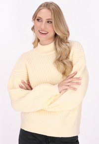 Żółty sweter ribbed z wysokim kołnierzem i szerokimi rękawami. Tekstura ma pionowe i ukośne wzory, co zwiększa jego wizualne zainteresowanie.