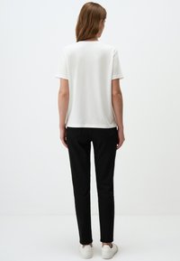 Witte T-shirt met korte mouwen en een ronde halslijn, gecombineerd met zwarte slim-fit broek en witte sneakers. Eenvoudig ontwerp, geen zichtbare patronen.