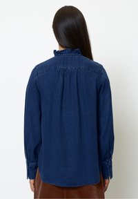 Donkerblauwe denim overhemd met lange mouwen, gerimpelde kraag, geplooide achterkant en knoopmanchetten. Gladde textuur en getailleerde pasvorm.