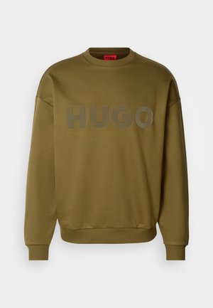 Olive roheline särk ümmarguse kaeluse, soonikute varrukate ja suure, mati logoga, kus on kirjutatud "HUGO" ees. Pehme tekstuur, mugav lõige.