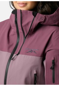 Veste imperméable dans une teinte prune avec un panneau prune plus clair. Caractéristiques : col montant, fermetures éclair noires et le logo "Swedemount". Deux poches zippées.