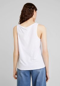 Vit ärmlös topp i bomull med rund hals och lös passform, tillsammans med blå vida denimbyxor.