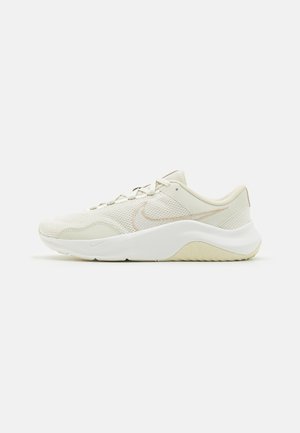 Zapatilla deportiva de malla beige con suela blanca gruesa, sutil logo swoosh, diseño con cordones y suela texturizada para un uso casual o deportivo.