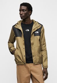 Μπεζ και μαύρο μπουφάν με κουκούλα και κούμπωμα με κουμπιά, διαθέτει ελαστικές μανσέτες και πλαϊνές τσέπες, συνδυασμένο με μαύρο μπλουζάκι.