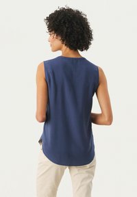 Marineblaue ärmellose Bluse mit Rundhalsausschnitt, glatter Textur und abgerundetem Saum. Seitliche Schlitze verbessern die Atmungsaktivität und Beweglichkeit.