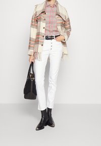 Beige rutigt jacka med fransar, röd rutigt skjorta, vita skinny jeans, svart bälte och spetsiga svarta stövlar. Svart handväska med detaljer.