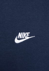 Tessuto di cotone blu navy con una texture liscia, caratterizzato da un logo Nike ricamato in bianco e il design dello swoosh. Estetica semplice e pulita.