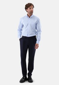 Camicia a righe azzurro chiaro e bianca con bottoni, abbinata a pantaloni blu scuro navy. L'outfit comprende scarpe nere e un design elegante.