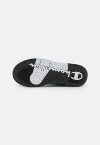 Sole di sneakers in bianco e nero con superficie in gomma testurizzata, logo "Champion" prominente e un accento circolare al centro.