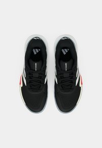 Μαύρα αθλητικά παπούτσια με άνω μέρος από δίχτυ, λευκές ρίγες, κόκκινες λεπτομέρειες και διαφανές πέλμα, με επενδεδυμένο γιακά και γλώσσα.