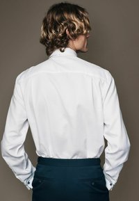 White button-up shirt with a textured fabric, featuring a pointed collar and cuffs with blue accents, paired with dark trousers.