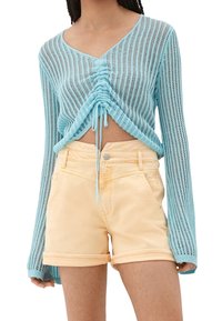 Suéter corto de punto azul claro con mangas largas y detalle de cordón en la parte delantera, combinado con pantalones cortos de denim amarillos.