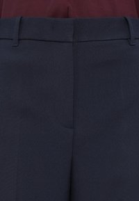 Close-up of navy blue tailored trousers with belt loops worn with a tucked-in dark red top.