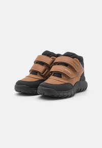 Scarpe in pelle marrone con suole in gomma nera e dettagli in rete, dotate di due cinturini in velcro per una facile regolazione e un design della punta arrotondata.