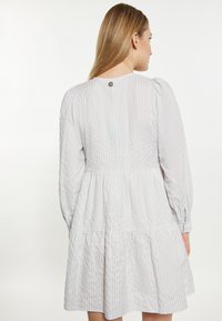 Abito bianco con strisce verticali azzurre chiare, maniche lunghe a sbuffo e gonna a strati. La chiusura con bottoni sul retro aggiunge un tocco di dettaglio.