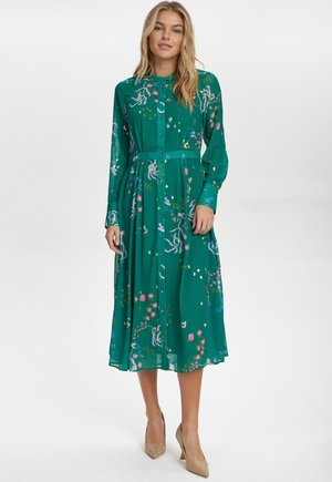 Abito verde con stampa floreale, maniche lunghe, chiusura con bottoni sul davanti e cintura in vita. Tessuto liscio con un design fluido di lunghezza intermedia.