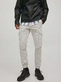 White cargo pants with elastic cuffs, made from cotton blend fabric. Styled with side pockets and paired with a black leather jacket.