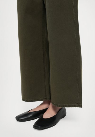 Zwarte platte schoenen met een ronde neus en een gladde textuur, gecombineerd met olijfgroene wijde broek met een afgewerkte zoom.