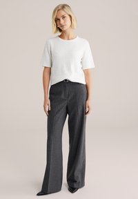 Biały fakturowany krótki top z krótkimi rękawami w zestawie z ciemnoszarymi szerokimi spodniami w prążki oraz czarnymi butami na szpic.