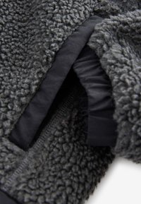 Close-up of dark gray textured fleece jacket showing zipper and inner black fabric lining.