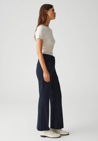 Navyblauwe formele broeken met een getailleerde pasvorm en brede pijpen, gecombineerd met een aansluitende witte T-shirt met korte mouwen en witte instapschoenen.