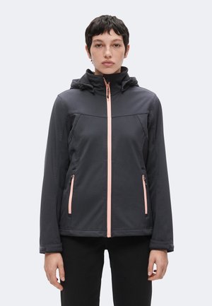 Persona che indossa una giacca nera con cappuccio, con zip rosa e dettagli sulle tasche, in piedi rivolta in avanti su uno sfondo semplice.