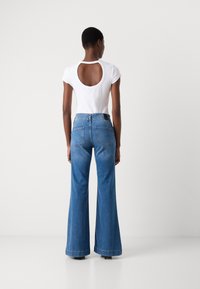 T-shirt blanc moulant avec un dos ouvert, associé à un jean flare bleu taille haute avec cinq poches et un léger délavage.