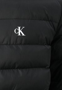 Must suurteks tahvliteks tikitud must talvejope, mille ülemisel küljel on valge "cK" logo. Valmistatud kergest ja siledast materjalist.