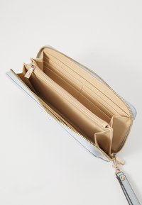 Portefeuille zippé bleu clair avec un extérieur texturé, plusieurs emplacements pour cartes, une poche centrale zippée et une doublure intérieure beige. Accents en métal doré.