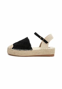 Espadrille de tejido negro trenzado con suela de yute, correa de tobillo ajustable y parte superior texturizada. Presenta un detalle de cuerda trenzada a lo largo de la suela.